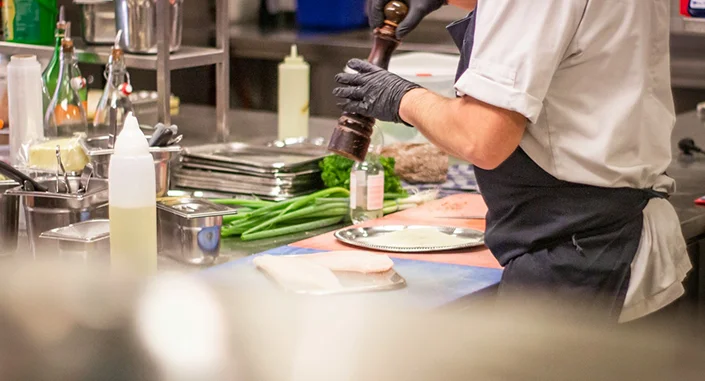 Professionele chef-kok die verse ingrediënten op smaak brengt terwijl hij een gerecht bereidt in een drukke restaurantkeuken.