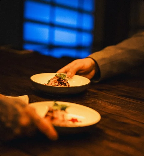 Close-up van twee elegant opgemaakte gerechten die worden geserveerd op een donkere houten restauranttafel in een warme, sfeervolle avondsetting.