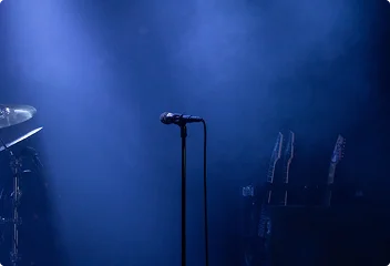 Sfeervolle live muziekpodium met een microfoon en instrumenten onder zacht blauw licht.