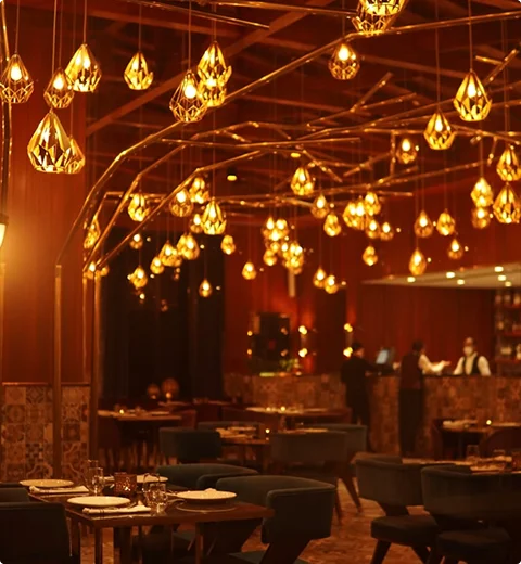 Stijlvol restaurantinterieur met decoratieve hanglampen, warme ambertonen en netjes gerangschikte eettafels.